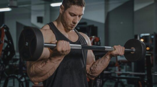 een bijzonder gespierde man die bicep curls aan het doen is (hij weet overduidelijk al hoelang het duurt om spieren te maken)